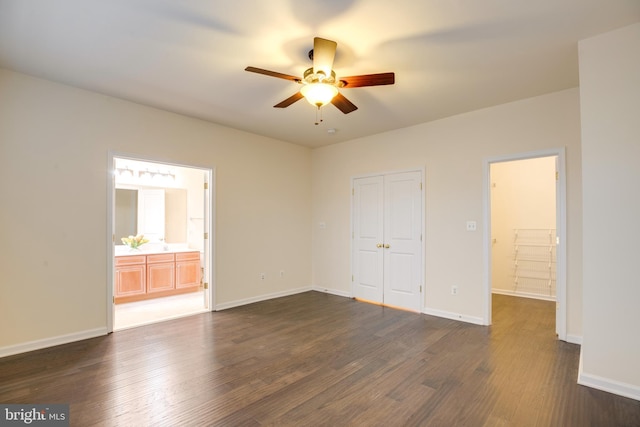 unfurnished bedroom featuring ceiling fan, dark wood-type flooring, ensuite bath, and a closet