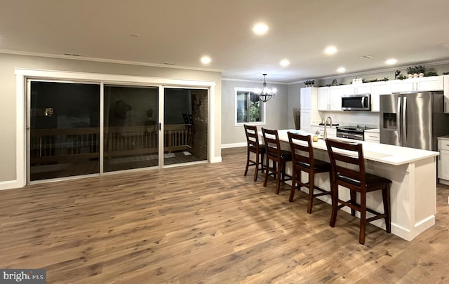 kitchen with a breakfast bar, an island with sink, wood-type flooring, white cabinets, and stainless steel appliances