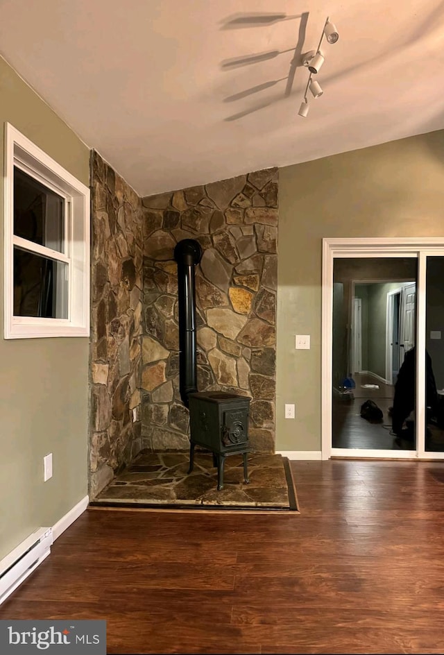 unfurnished living room with wood-type flooring, a wood stove, and a baseboard heating unit