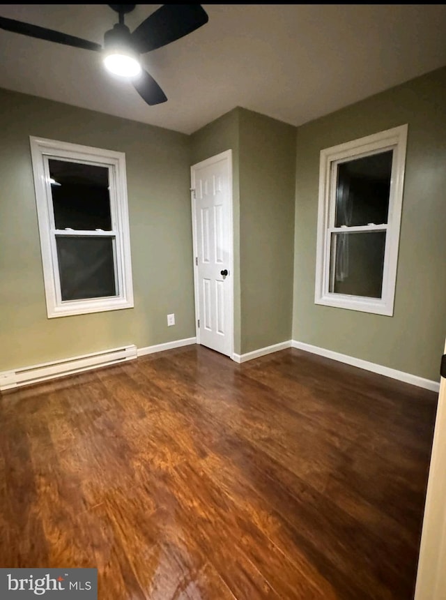 empty room featuring baseboard heating, ceiling fan, and dark hardwood / wood-style floors