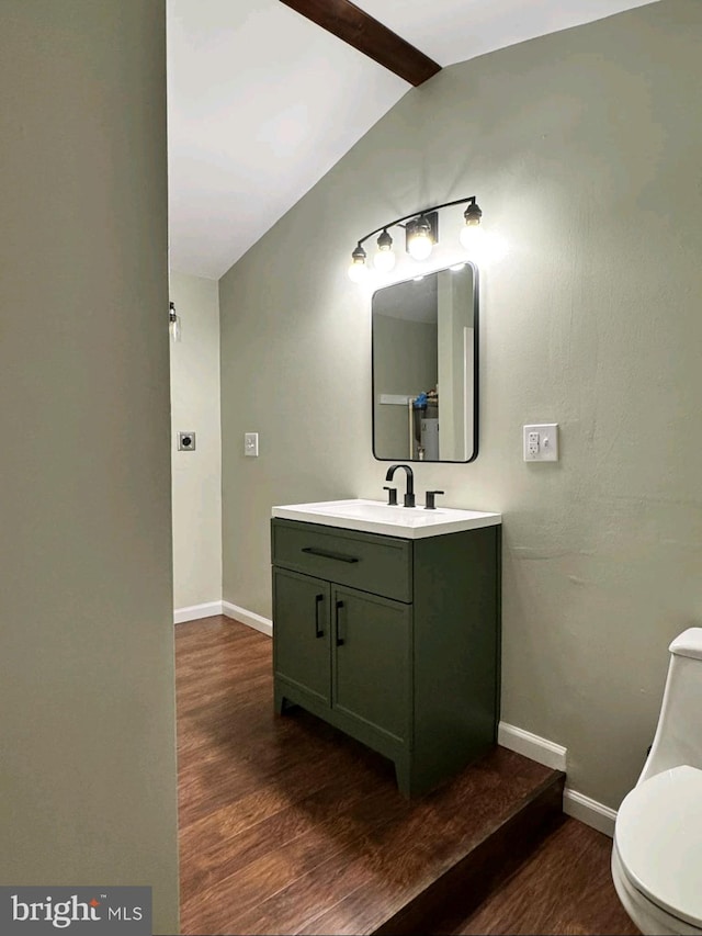 bathroom featuring vanity, toilet, hardwood / wood-style floors, and vaulted ceiling with beams