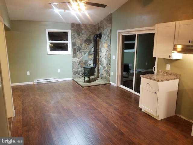 unfurnished living room featuring ceiling fan, a baseboard heating unit, dark hardwood / wood-style flooring, vaulted ceiling, and a wood stove