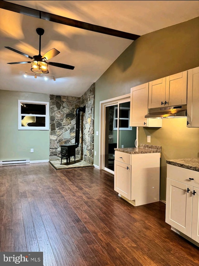 kitchen featuring vaulted ceiling, a wood stove, dark stone countertops, and white cabinets