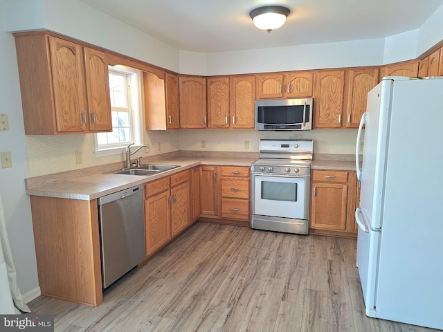 kitchen with appliances with stainless steel finishes, sink, and light hardwood / wood-style flooring