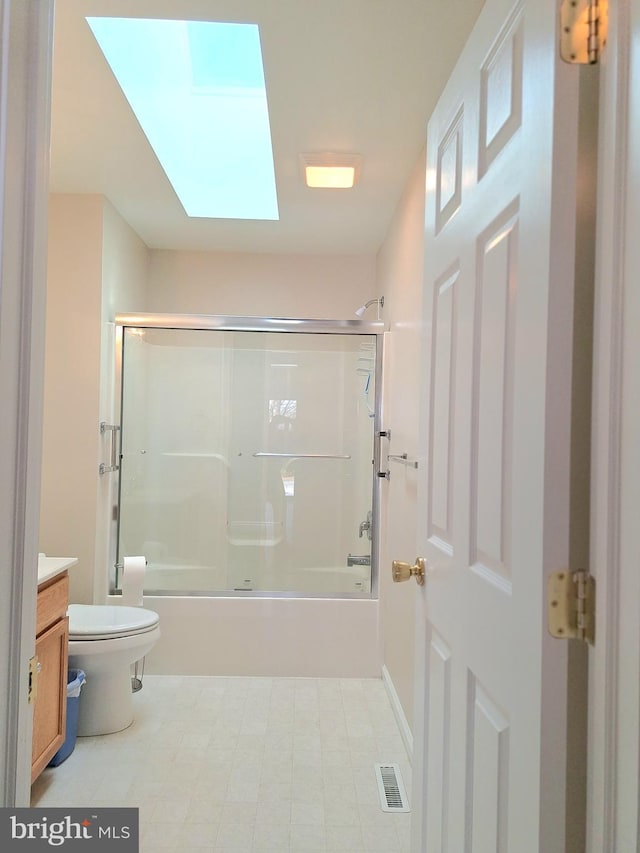 full bathroom featuring vanity, a skylight, bath / shower combo with glass door, and toilet