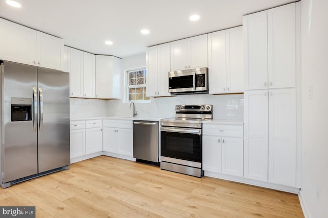 kitchen with white cabinetry, appliances with stainless steel finishes, light hardwood / wood-style floors, and decorative backsplash