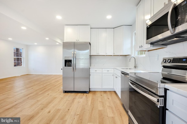 kitchen with sink, white cabinetry, tasteful backsplash, appliances with stainless steel finishes, and light hardwood / wood-style floors