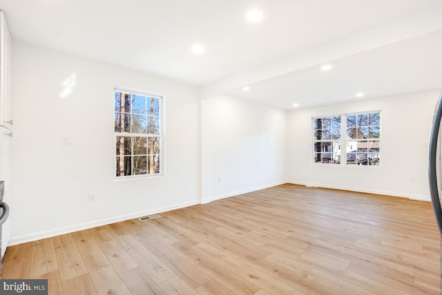 unfurnished room with beam ceiling, a wealth of natural light, and light hardwood / wood-style floors