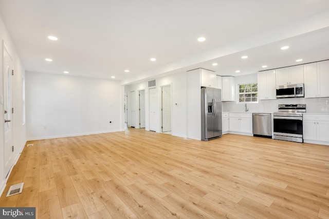 kitchen with stainless steel appliances, white cabinetry, and light hardwood / wood-style floors