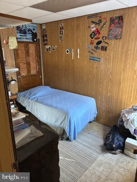 bedroom featuring a paneled ceiling and wood walls