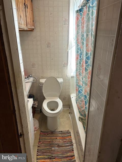 bathroom featuring toilet, tile patterned floors, shower / bathtub combination with curtain, and tile walls