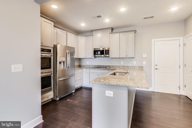 kitchen with sink, appliances with stainless steel finishes, light stone counters, a kitchen bar, and kitchen peninsula