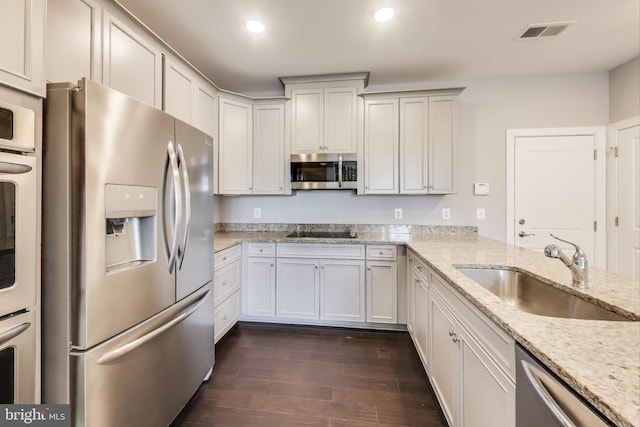 kitchen featuring sink, appliances with stainless steel finishes, dark hardwood / wood-style floors, light stone countertops, and white cabinets