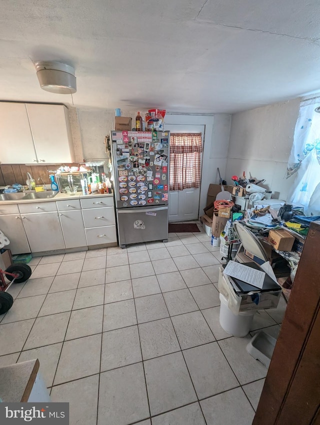 kitchen with stainless steel refrigerator, light tile patterned floors, sink, and white cabinets