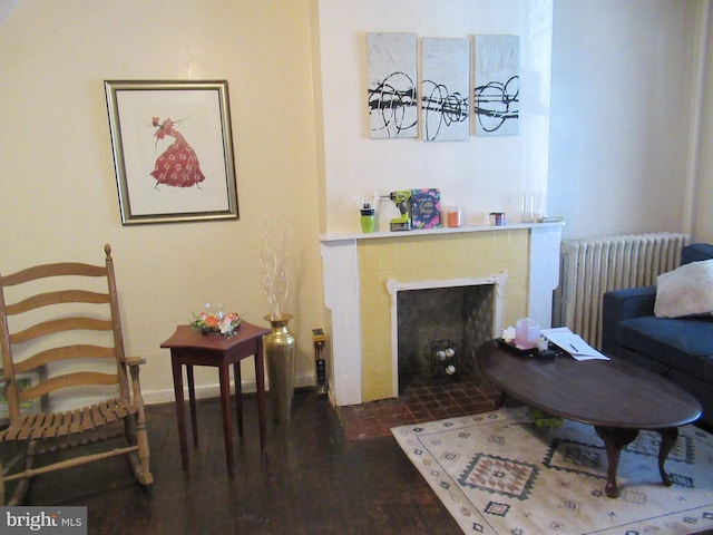 living area with radiator heating unit, dark hardwood / wood-style flooring, and a brick fireplace