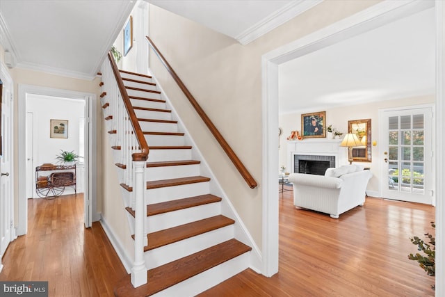 staircase with hardwood / wood-style flooring, ornamental molding, and a brick fireplace