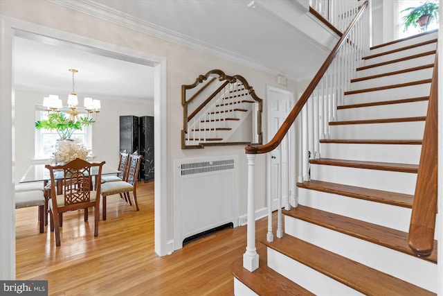 staircase with hardwood / wood-style floors, crown molding, radiator heating unit, and a chandelier