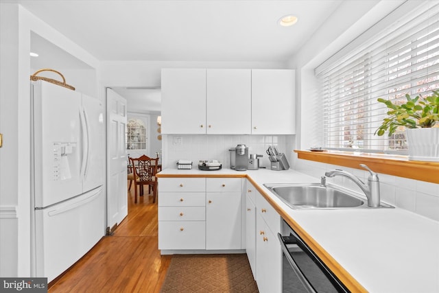 kitchen with sink, white cabinetry, light wood-type flooring, white fridge with ice dispenser, and backsplash