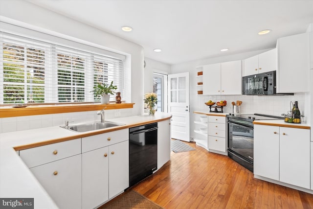 kitchen with sink, backsplash, white cabinets, black appliances, and light wood-type flooring