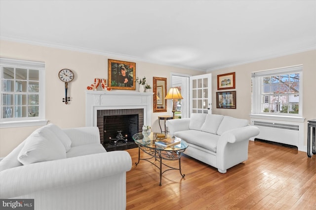 living room with radiator, crown molding, light hardwood / wood-style flooring, and a brick fireplace