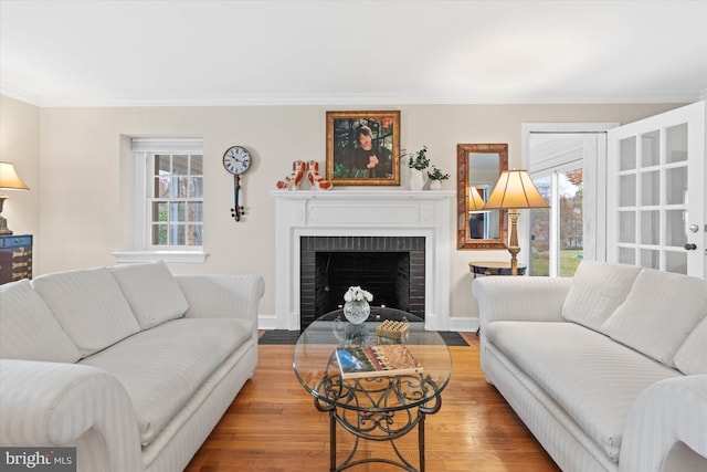 living room with a brick fireplace, crown molding, a wealth of natural light, and light wood-type flooring