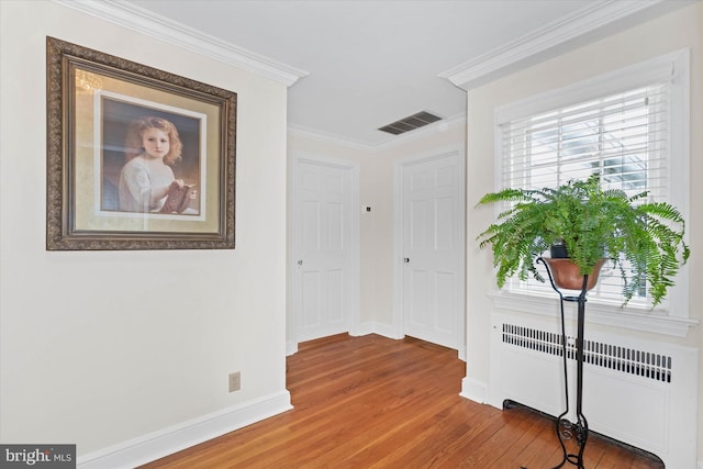 corridor with crown molding, radiator heating unit, and wood-type flooring