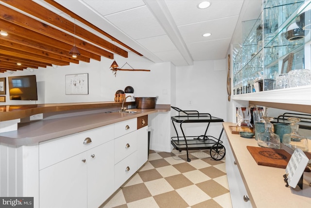 kitchen with sink, white cabinets, and beam ceiling