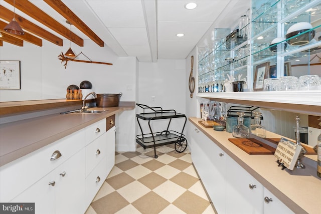 interior space with white cabinetry, sink, and beam ceiling