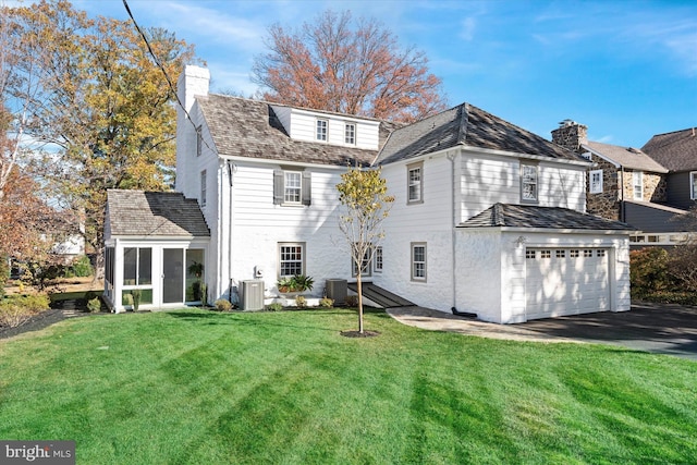 back of property featuring a yard, a garage, a sunroom, and central air condition unit