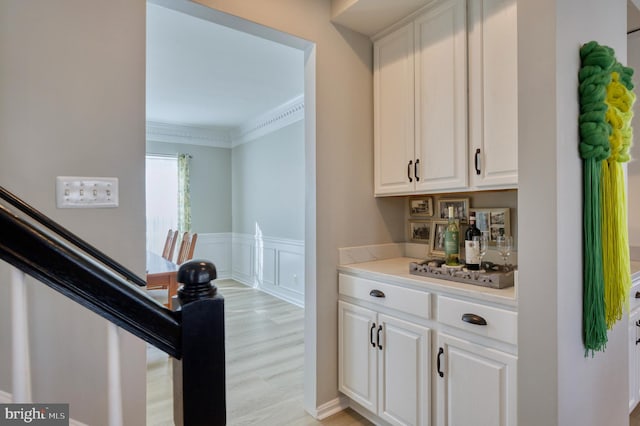 bar with white cabinetry, crown molding, and light hardwood / wood-style floors