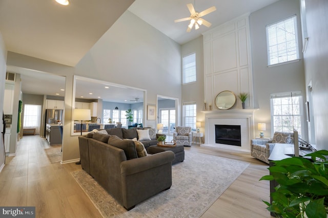 living room featuring a fireplace, light hardwood / wood-style flooring, ceiling fan, and a high ceiling