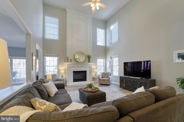 living room featuring a towering ceiling, light hardwood / wood-style floors, a large fireplace, and ceiling fan