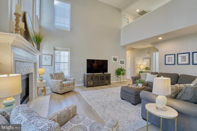 living room with a fireplace, a high ceiling, and light wood-type flooring