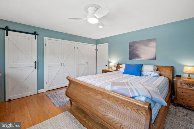 bedroom featuring ceiling fan, two closets, light wood-type flooring, and a barn door