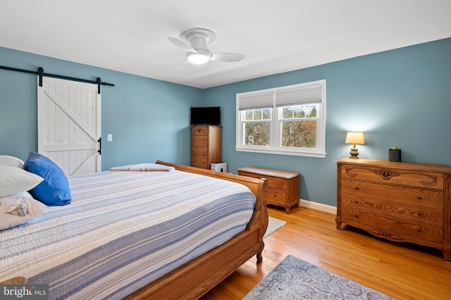 bedroom with ceiling fan, a barn door, baseboards, and wood finished floors