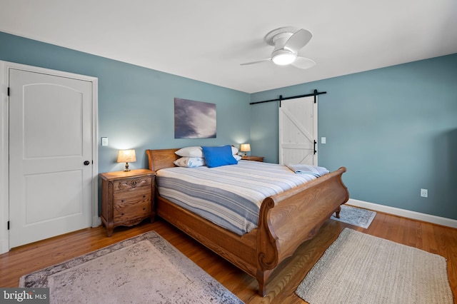 bedroom featuring ceiling fan, a barn door, baseboards, and wood finished floors