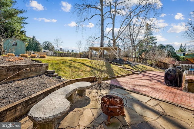 view of patio featuring a storage shed, an outbuilding, a fire pit, and a fenced backyard