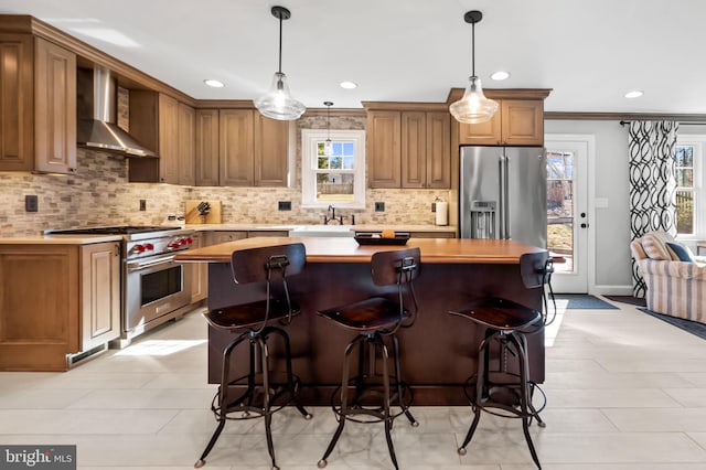 kitchen with appliances with stainless steel finishes, a center island, light countertops, and wall chimney range hood