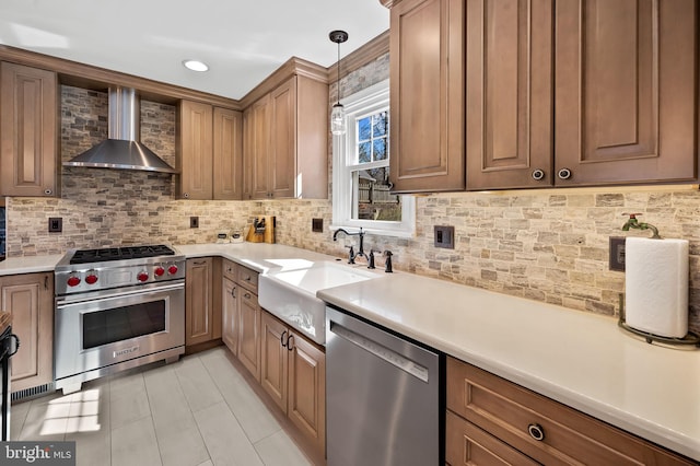 kitchen featuring a sink, appliances with stainless steel finishes, wall chimney range hood, decorative light fixtures, and tasteful backsplash