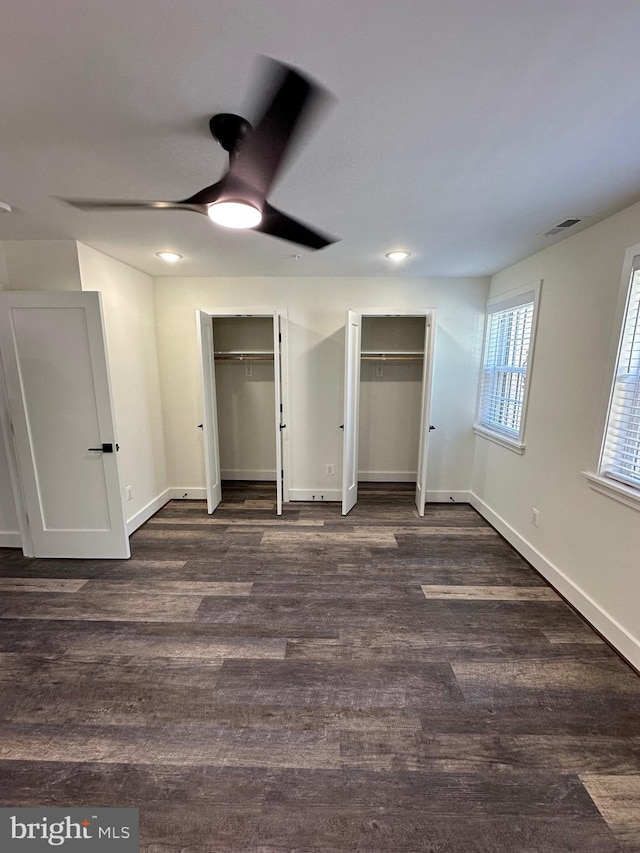 unfurnished bedroom featuring dark wood-type flooring, two closets, and ceiling fan