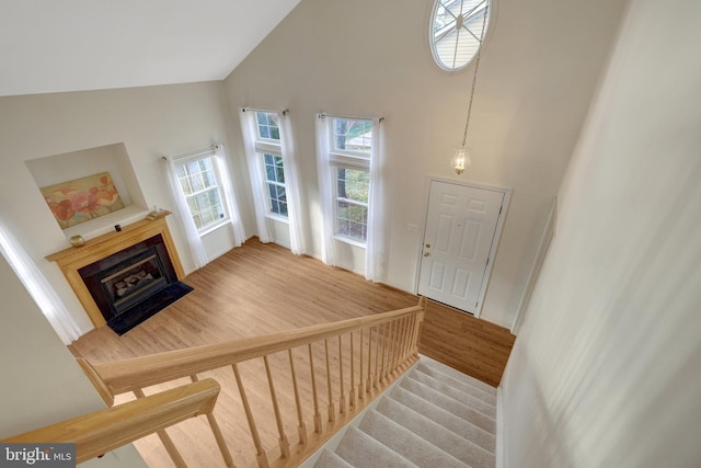 staircase featuring high vaulted ceiling, wood finished floors, and a glass covered fireplace