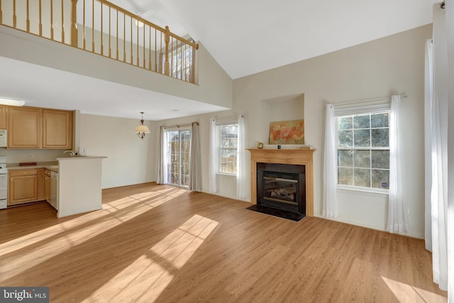 unfurnished living room featuring light wood-type flooring, a fireplace with flush hearth, and a towering ceiling