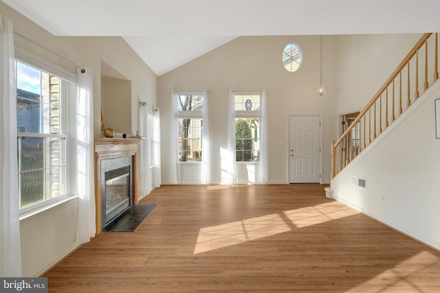 unfurnished living room featuring visible vents, light wood-style flooring, a premium fireplace, stairway, and high vaulted ceiling