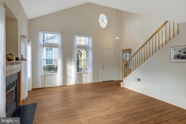 living room featuring a fireplace with flush hearth, wood finished floors, visible vents, and stairs