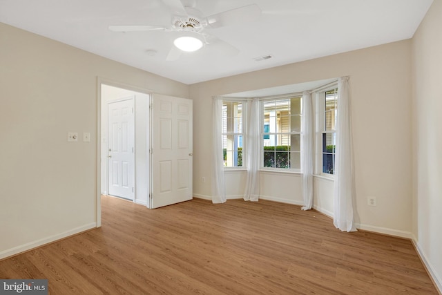 empty room featuring light wood-style floors, baseboards, visible vents, and a ceiling fan