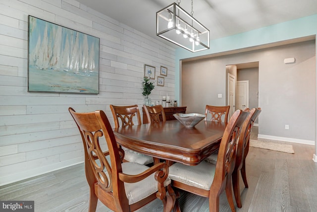 dining space with an inviting chandelier, hardwood / wood-style floors, and wooden walls