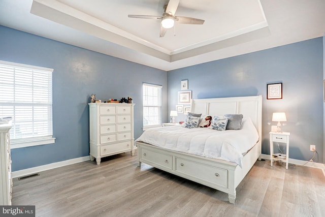 bedroom with a tray ceiling, ceiling fan, and light wood-type flooring