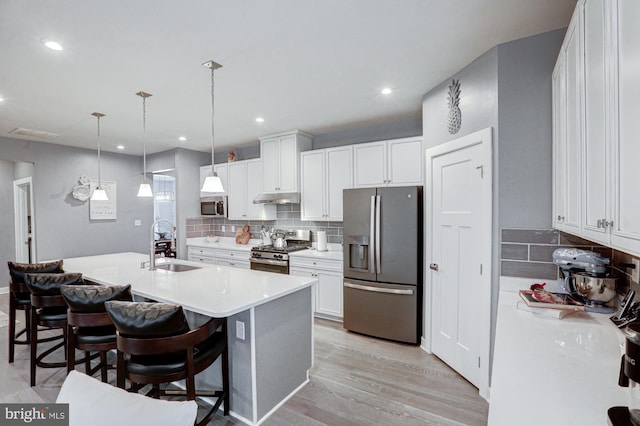 kitchen with sink, a breakfast bar area, white cabinetry, decorative light fixtures, and stainless steel appliances