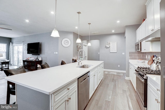 kitchen featuring sink, white cabinetry, hanging light fixtures, a center island with sink, and appliances with stainless steel finishes