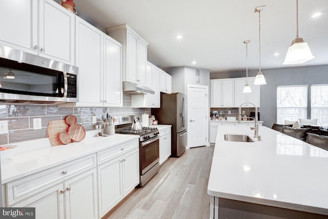 kitchen with appliances with stainless steel finishes, decorative light fixtures, sink, white cabinets, and backsplash